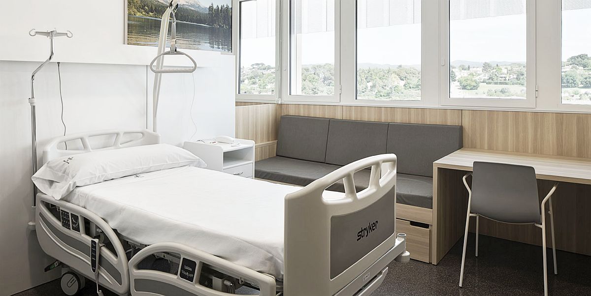 Com ingressar: detall de l'habitació d'un pacient, amb llit reclinable, sofà, taula i vistes a l'exterior